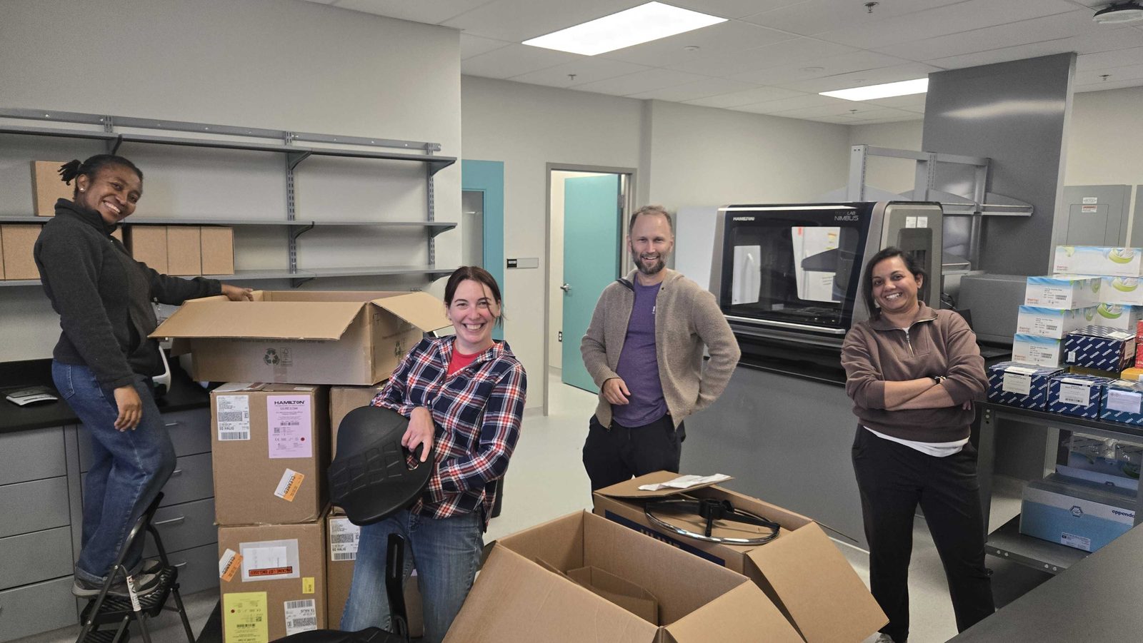 Four lab members smiling while unpacking boxes in the new lab